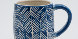 handmade ceramic mug with cuerda seca decoration, navy blue and white geometric pattern, dark wax resist outlines, matte glaze, studio pottery, clean white background, product photography